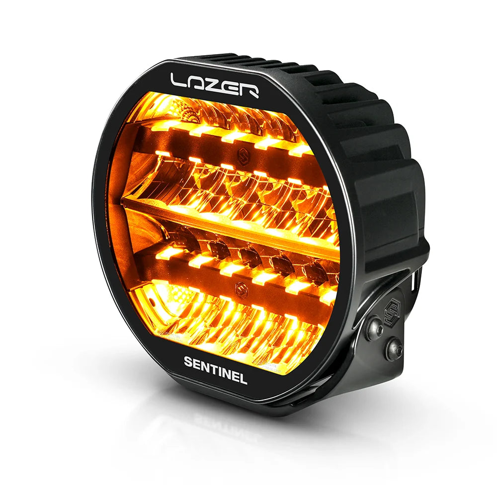 Musta 9-tuumainen Lazer Sentinel Highline -lisävalo, jossa on pyöreä muotoilu, oranssit LED-parkkivalot, heijastimet useassa rivissä ja jäähdytysrivat taustalla. Valo on valkoista taustaa vasten ja kuvattu yläviistosta.