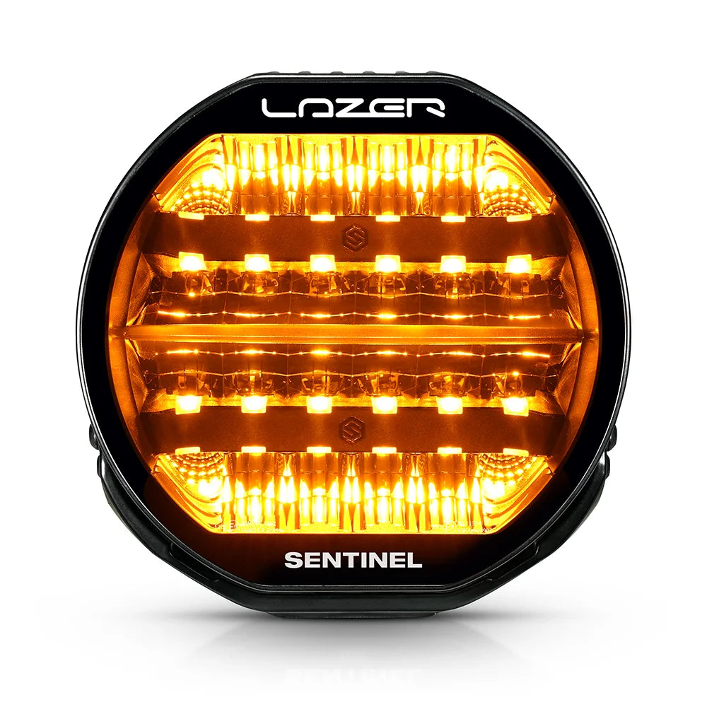 Musta 9-tuumainen Lazer Sentinel Highline -lisävalo, jossa on pyöreä muotoilu, oranssit LED-parkkivalot, heijastimet useassa rivissä ja jäähdytysrivat taustalla. Valo on valkoista taustaa vasten ja kuvattu edestä.