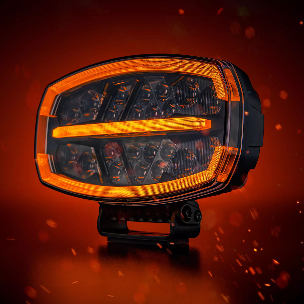 Strands Firefly One Ovalin muotoinen lisävalo punaisella taustalla missä kipinöitä. Valon ylä, sekä alareunassa ja keskellä oranssit parkit, sekä valon sisäpinta useille pyöreillä heijastinelementeillä.