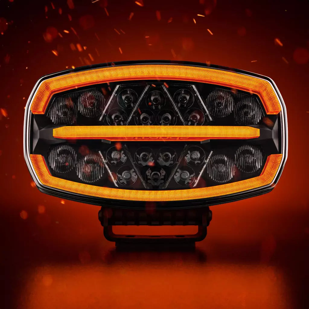 Strands Firefly One Ovalin muotoinen lisävalo punaisella taustalla missä kipinöitä. Valon ylä, sekä alareunassa ja keskellä oranssit parkit, sekä valon sisäpinta useille pyöreillä heijastinelementeillä. Valo kuvattu suoraan edestä päin