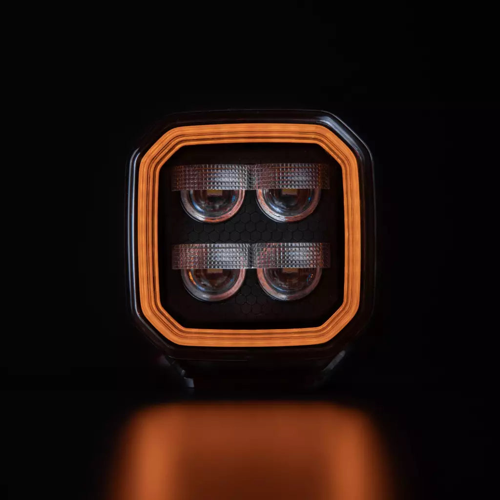 Strands For9t häikäisemätön led-työvalo mustaa taustaa vasten ja oranssi upea parkki kiertää valon sisäpintaa neljässä eri tasossa. Keskellä neljä eri heijastinelementtiä. Valo on muodoltaan neliö ja leikatut kulmat. Valo kuvattu suoraan edestä päin.