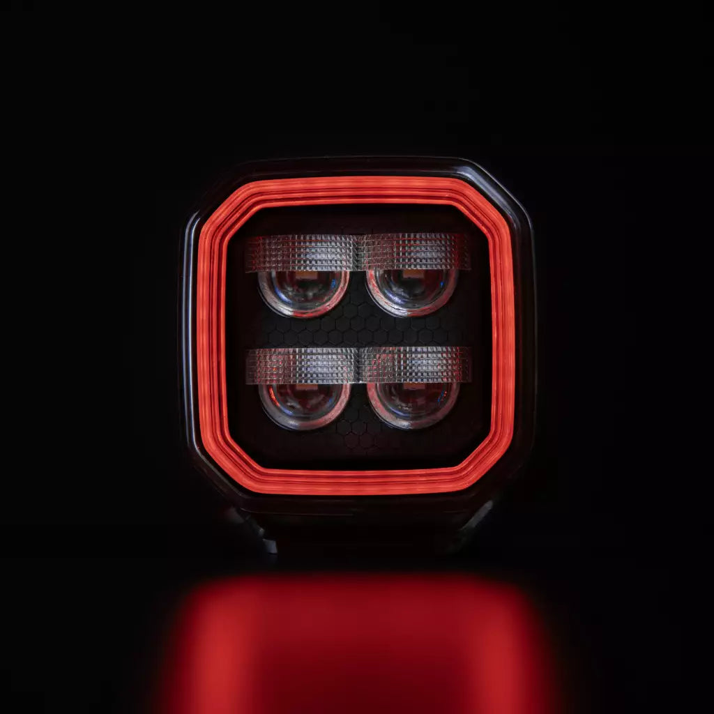 Strands For9t häikäisemätön led-työvalo mustaa taustaa vasten ja upea punainen parkki kiertää valon sisäpintaa neljässä eri tasossa. Keskellä neljä eri heijastinelementtiä. Valo on muodoltaan neliö ja leikatut kulmat. Valo kuvattu suoraan edestä päin