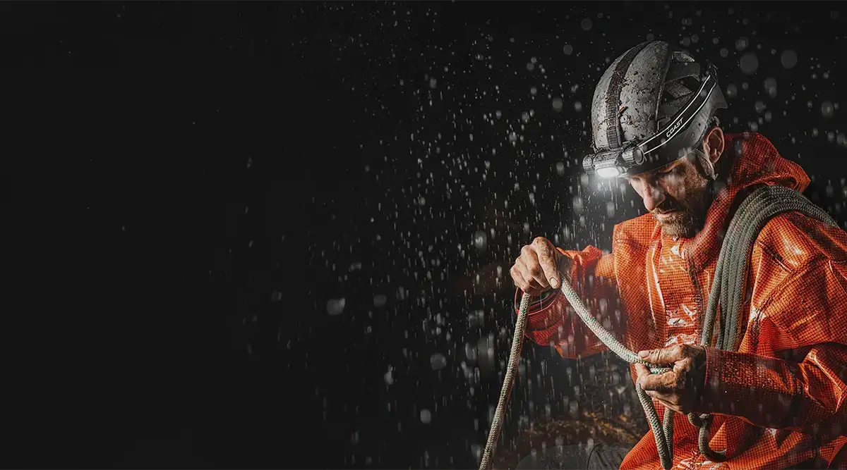 Tehokas Coast otsalamppu kypärään kiinnitettynä ja mies työskentelee narun kanssa vesisateessa.