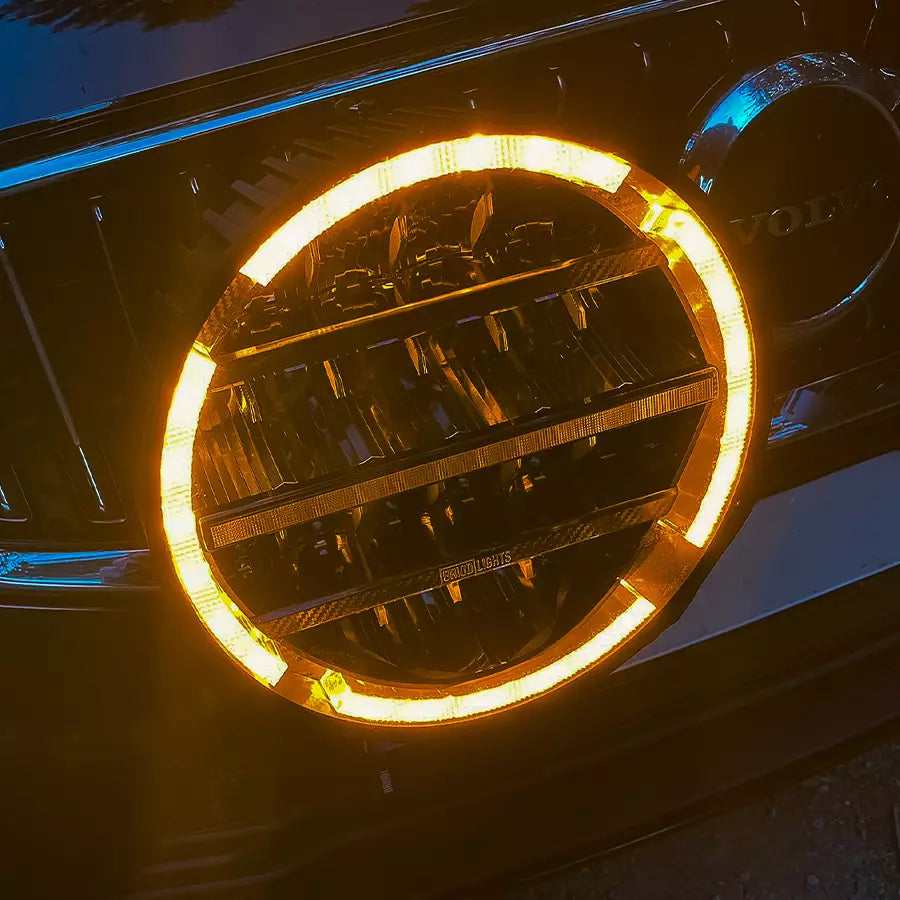 BriodLights Olympus 9-tuumainen pyöreä lisävalo asennettuna henkilöauton keulalle. Valossa päällä oranssit parkkivalot. Kuvattu yläviistosta.